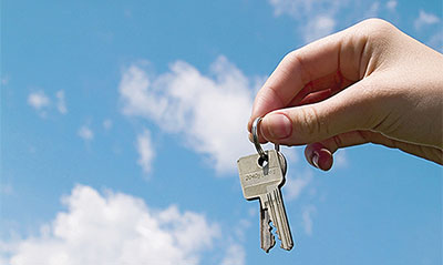 Woman holding up some keys with the sky in the background